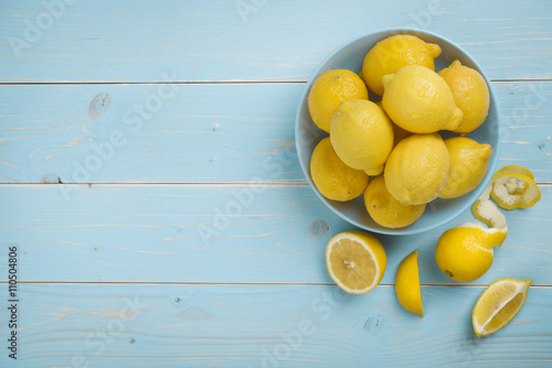 Bowl with fresh lemons on blue wooden background. Top view