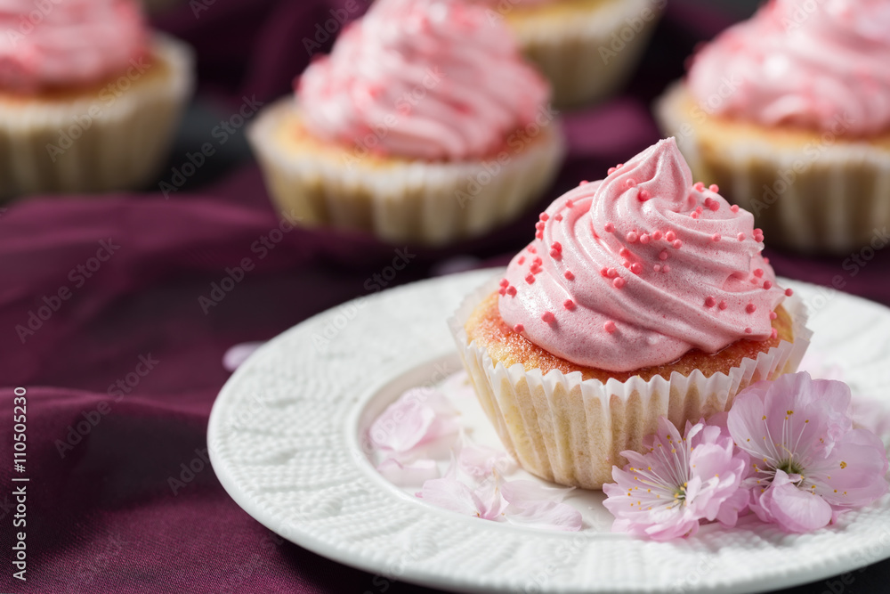 Vanilla cupcakes with pink cream on dark purple background, pink flower, text space selective focus, close up
