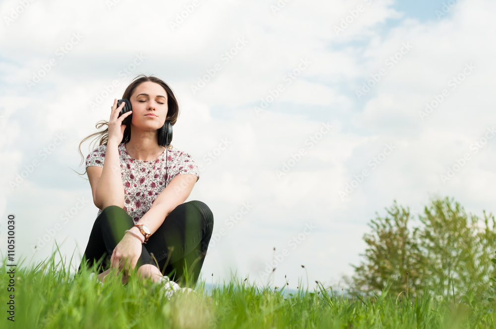 Enjoying music concept with young female sitting outside with ea Enjoying music concept with young female sitting outside with ea