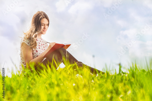 Beautiful female sitting and on green meadow and writing