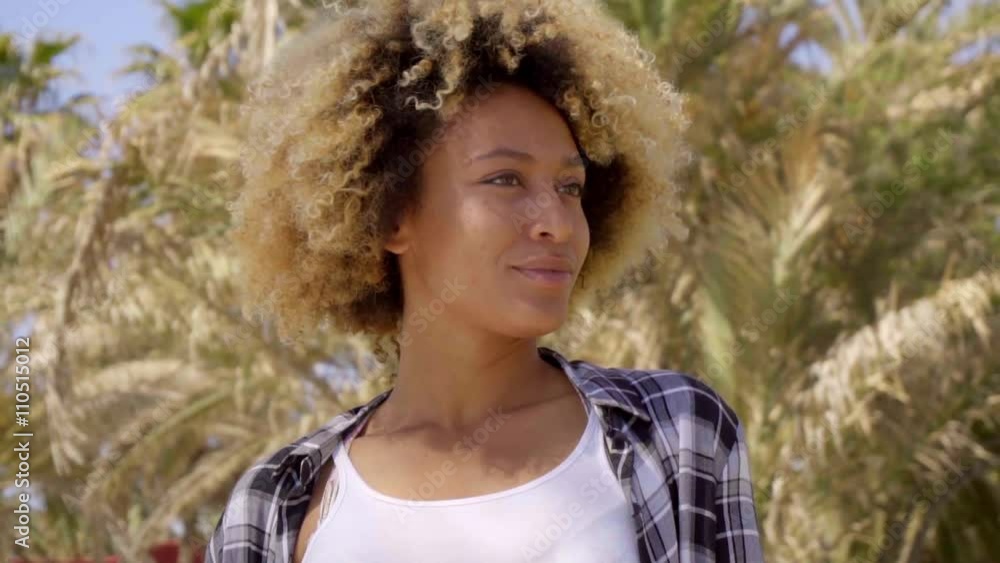 Close up of young woman with tight blond curls turned away from camera besides palm trees under a bright summer sun Close up of young woman with tight blond curls turned away from camera besides palm trees under a bright summer sun