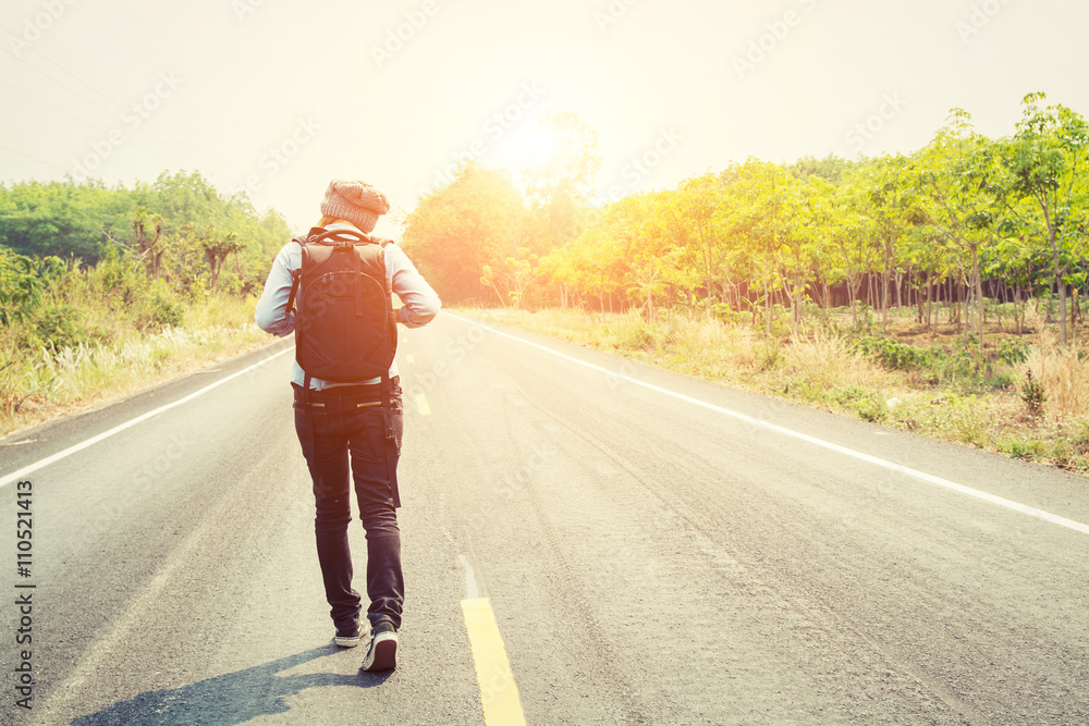 Fototapeta premium Rear view of a young woman hitchhiking carrying backpack walking