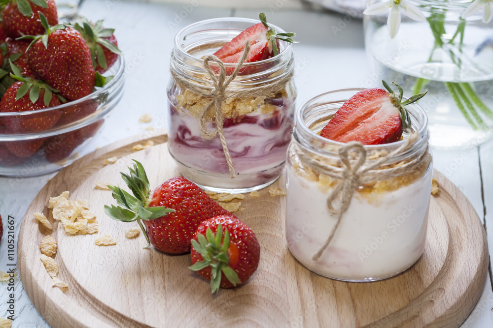Homemade healthy dessert in a glass with yogurt, fresh strawberry and corn flakes for breakfast with fresh white flowers on wooden table, closeup Homemade healthy dessert in a glass with yogurt, fresh strawberry and corn flakes for breakfast with fresh white flowers on wooden table, closeup