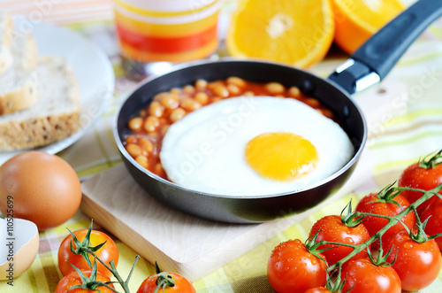 Fried egg with beans, toast bread, fresh juice, tomatoes and oranges