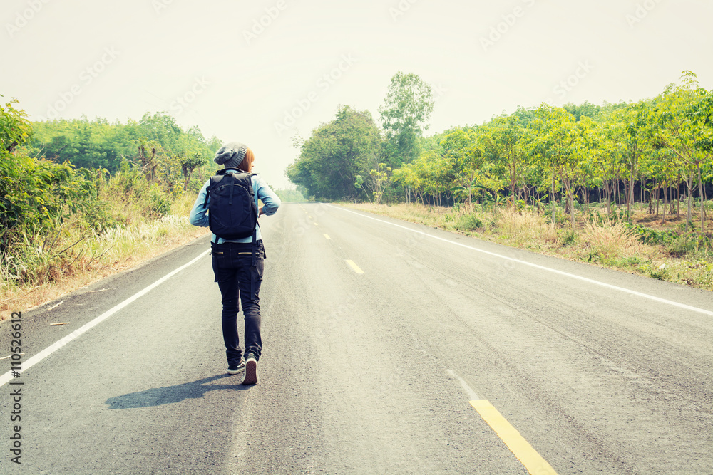 Rear view of a young woman hitchhiking carrying backpack walking