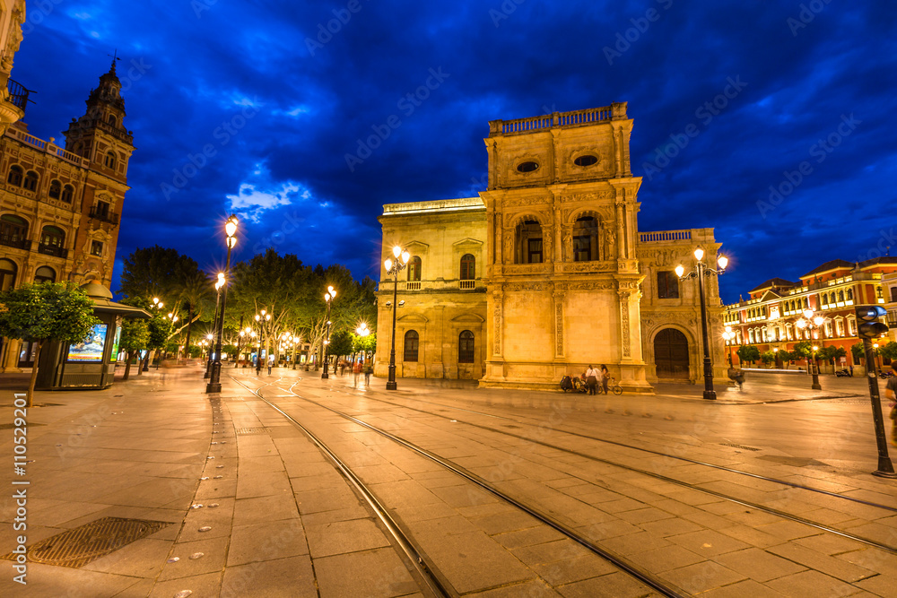 Tram tracks, historic buildings and the streets of the center of Seville illuminated by night. Seville town, Andalusia, Spain.