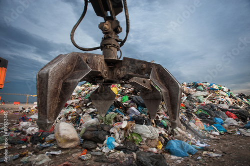 Close up of mechanical arm grabbing waste from a pile at city landfill photo