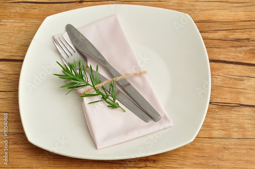 A simple place setting consisting of a plate and a knife and fork with a napkin that is tied together an empty name card  © Marietjie Opperman