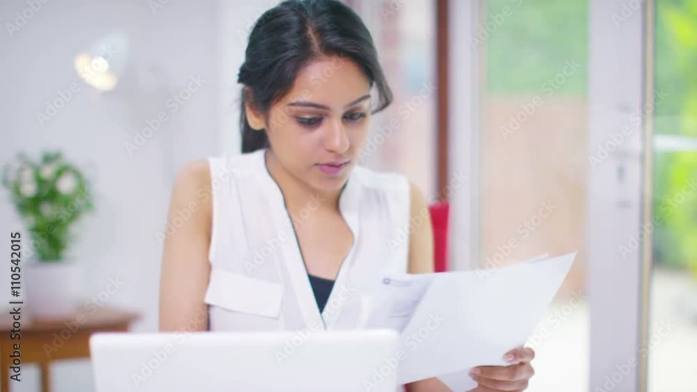 Cheerful young woman working on a laptop computer & looking at paperwork Cheerful young woman working on a laptop computer & looking at paperwork