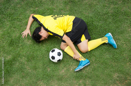 Football player in Yellow lying injured on the pitch.