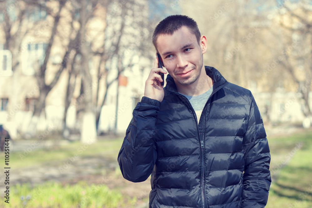 The young successful man with a mobile phone on the background of the spring streetscape .