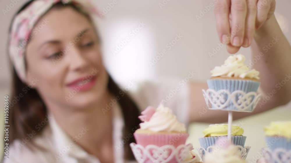 Smiling woman with bakery business putting finishing touches onto cupcakes Smiling woman with bakery business putting finishing touches onto cupcakes