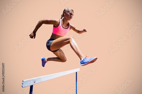 Composite image of sporty woman jumping a hurdle