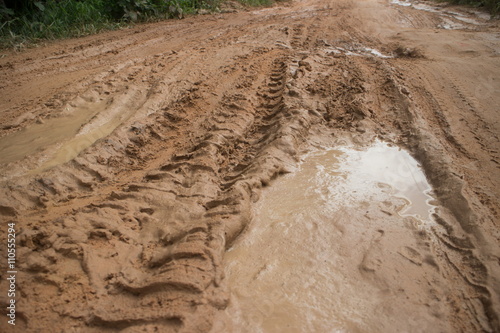 Wider ground level view horizontal MCU muddy jungle road with muddy tire track and side vegetation