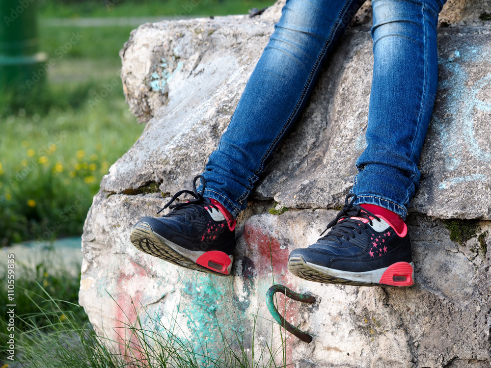 Obraz premium Legs of a teenager. Jeans, sneakers. Old dirty concrete wall. The concept - nature of adolescent behavior. Green grass