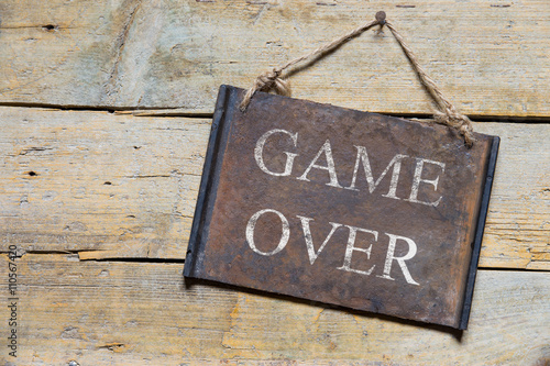 rusty metal sign on wooden table, text game over