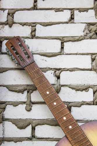 Acoustic guitar headstock against white brick wall © zimnevan
