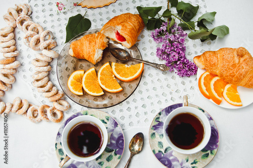 Beautiful and healthy Breakfast: croissants and coffee on the table with oranges and lilac flowers