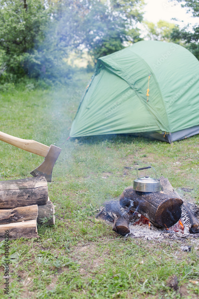 Camping in the woods with a fire ax and a tent. - obrazy, fototapety, plakaty 