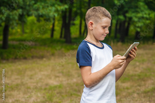 Cute young caucasian kid working with tablet in park.