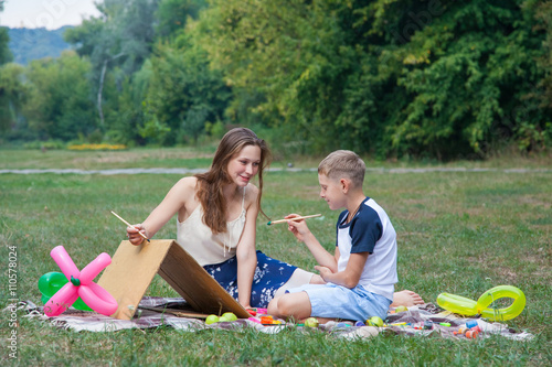 Older sister trying to teach her brother to paint in the park