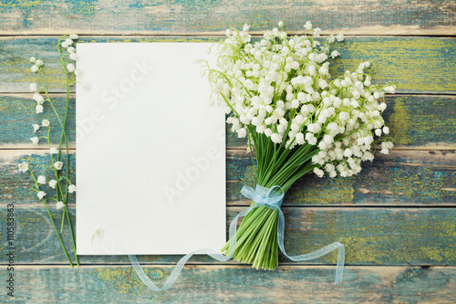 Bouquet of flowers lily of the valley and empty paper sheet on rustic table from above, beautiful vintage card, top view, copy space for text, flat lay