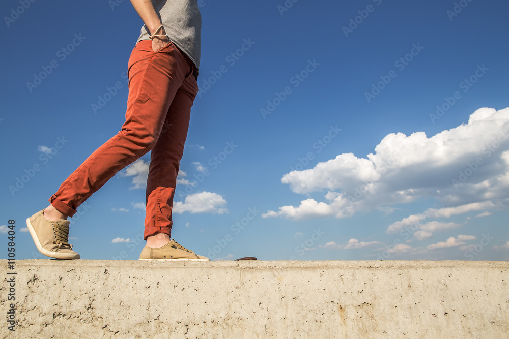 people comfortably saunters on a sunny warm day on a concrete wall holding the her hands in their pockets against blue sky background and white clouds people comfortably saunters on a sunny warm day on a concrete wall holding the her hands in their pockets against blue sky background and white clouds