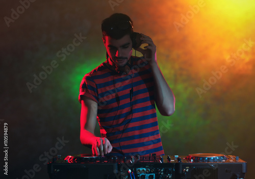 DJ playing music at mixer on colorful blurred background