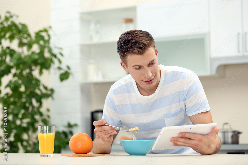 Handsome man with tablet and having breakfast in kitchen Handsome man with tablet and having breakfast in kitchen