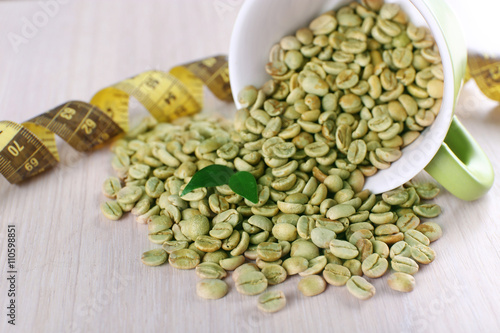 Green coffee beans in a cup with measuring tape on white wooden table