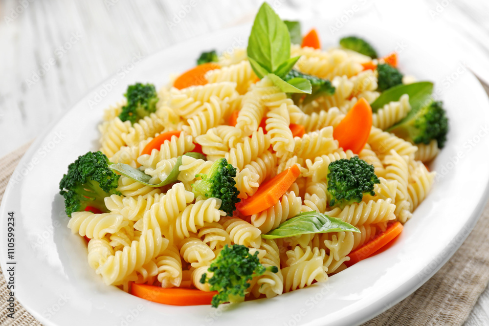 Boiled fusilli pasta with carrot, broccoli and basil on white plate Boiled fusilli pasta with carrot, broccoli and basil on white plate