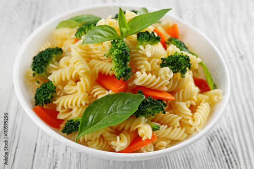 Boiled fusilli pasta with carrot, broccoli and basil on white plate