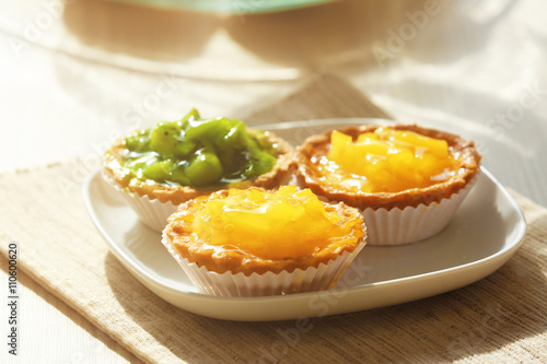 Fresh homemade fruit tarts with citruses and kiwi on a white table.