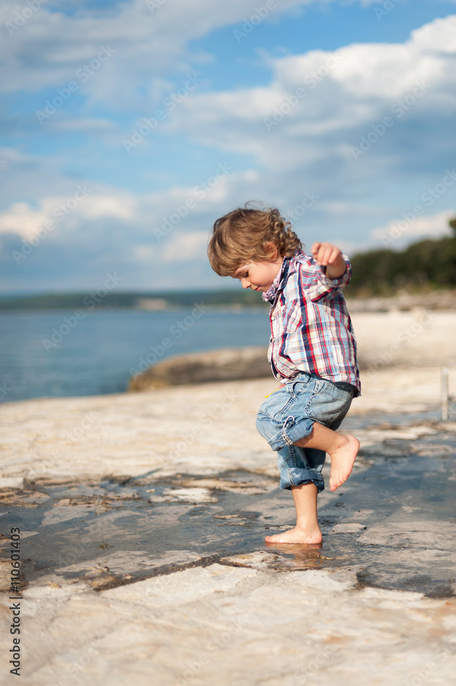 Cute little boy on the beach having fun playing and jumping in a puddle of seawater. Cute little boy on the beach having fun playing and jumping in a puddle of seawater.