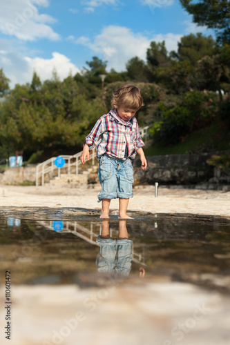 Cute little boy on the beach having fun playing and jumping in a puddle of seawater. Reflection in a water.