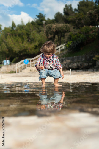 Fototapeta Naklejka Na Ścianę i Meble -  Cute little boy on the beach having fun playing and jumping in a puddle of seawater. Reflection in a puddle.