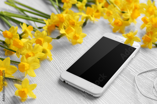Fresh narcissus flowers with mobile phone and earphones on wooden background
