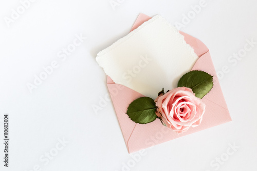 Pink envelop with white card and rose. Flat lay.