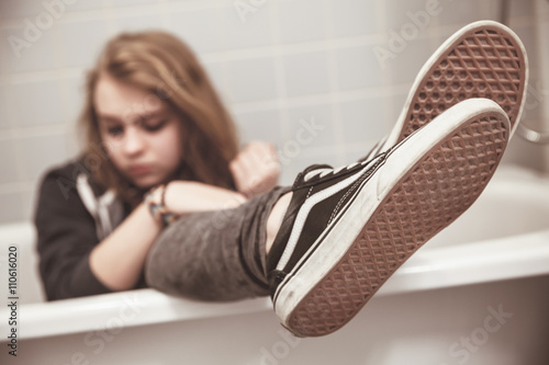 Teenage girl in black sneakers sits in bath