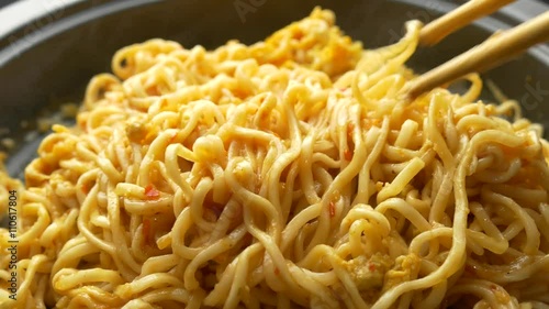 close up of chopsticks stirring cooking instant noodles in frying pan