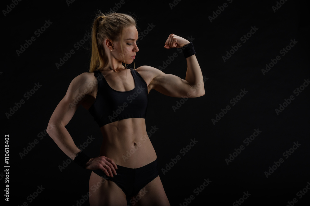 Obraz premium Young muscular woman posing on black