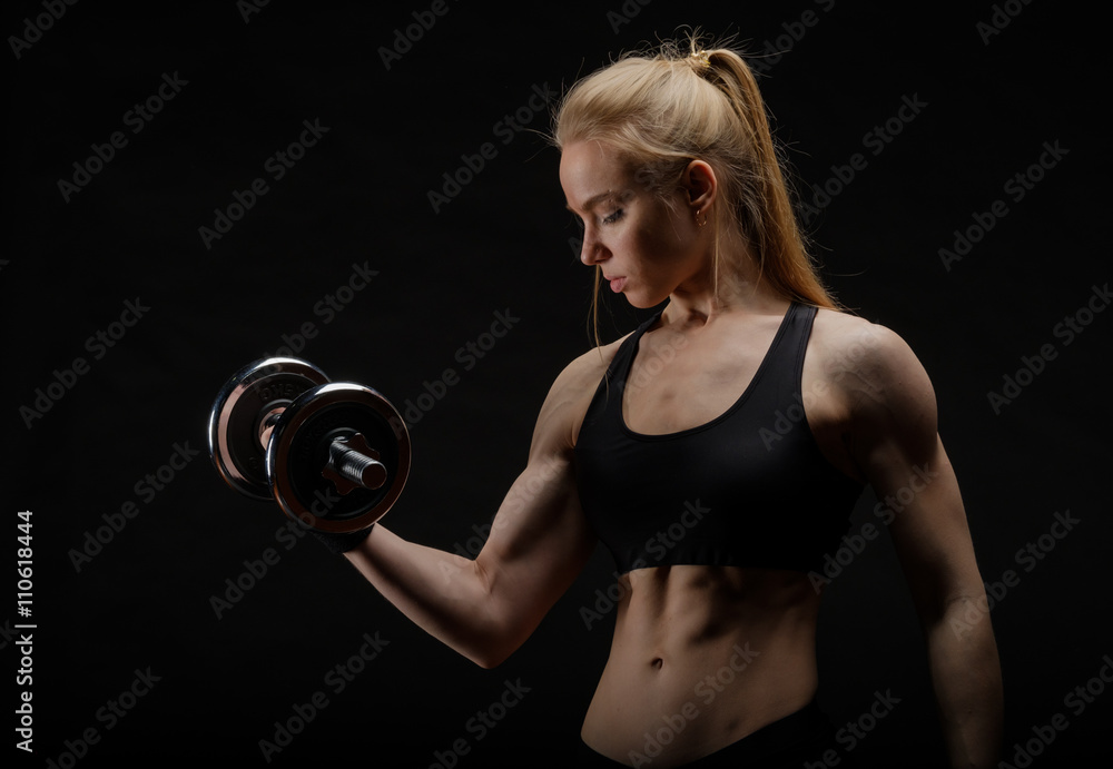 Young slim strong muscular woman posing in studio with dumbbell Young slim strong muscular woman posing in studio with dumbbell