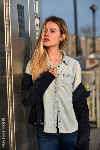 Fashion urban portrait of young, slim, beautiful model in denim shirt and jeans posing against metallic background.
