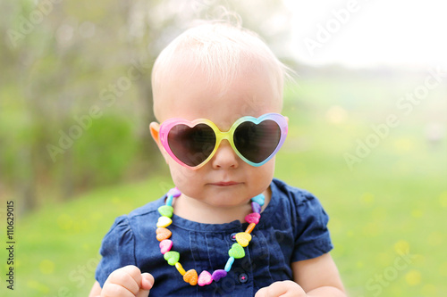 Cute one year old baby girl wearing heart shaped sunglasses and necklace outside on a sunny summer day. photo