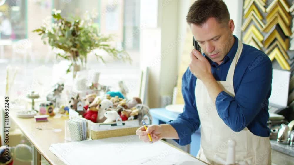 Cheerful business owner makes a phone call behind the counter of his shop Cheerful business owner makes a phone call behind the counter of his shop