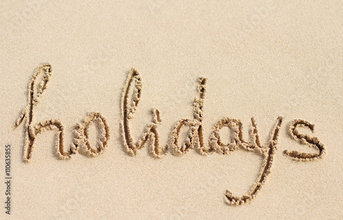 Word Holidays handwritten on sand