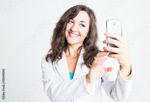 Beautiful lady in white jacket making a photo on telephone isolated on white background