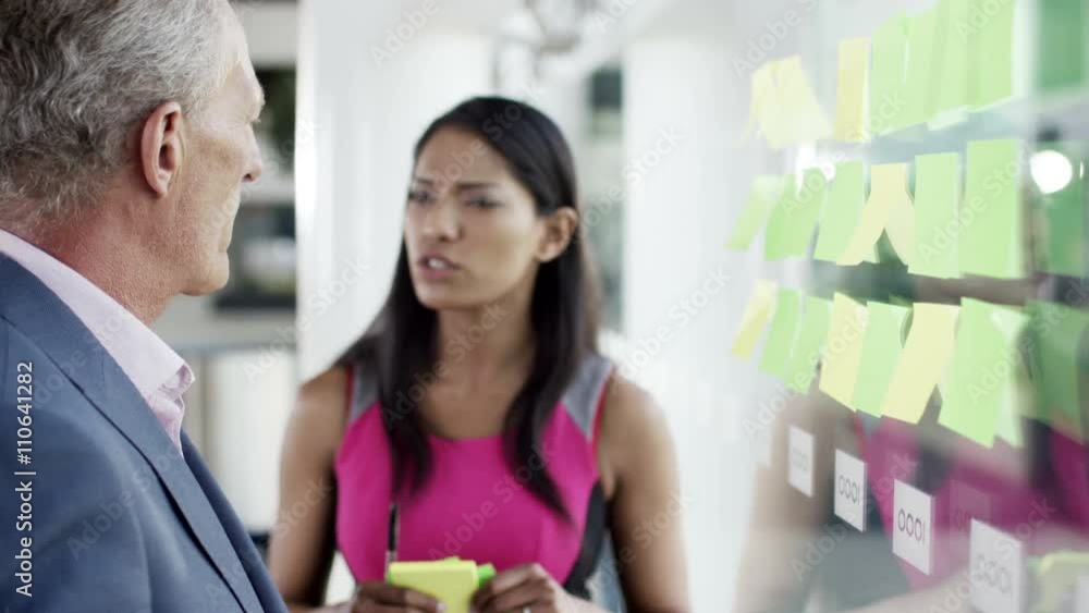 Attractive business man and woman brainstorming for ideas with sticky notes Attractive business man and woman brainstorming for ideas with sticky notes