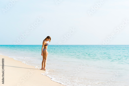 Young beautiful woman in swimwear standing alone on the beach.