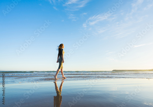 Young woman in dress walk on the beach at sunset time.
